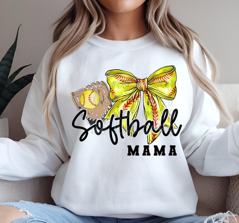 May include: White sweatshirt with a yellow and red softball bow, a softball glove, and the text "Softball Mama".