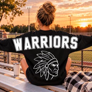 May include: A black long-sleeve sweatshirt featuring the word WARRIORS in large white block letters across the upper back, with a white graphic illustration of a person wearing a feathered headdress positioned below the text.
