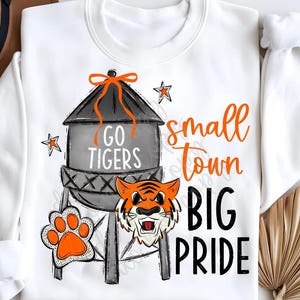 May include: White sweatshirt with a black and gray water tower graphic, a tiger mascot, and the text "Go Tigers", "Small Town Big Pride".