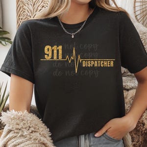 Puede incluir: Camiseta negra con texto en purpurina dorada y un gráfico de latido del corazón que dice "911 Dispatcher".