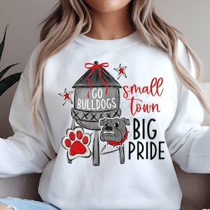 May include: White sweatshirt with a graphic design featuring a water tower with the text "Go Bulldogs", a paw print, a bulldog, and the text "Small Town Big Pride".
