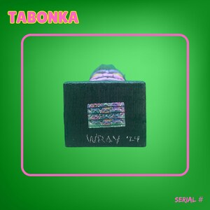 May include: A wooden figurine with a colorful, layered design. The figurine is on a black base with a holographic sticker and the text "Infinity '24".