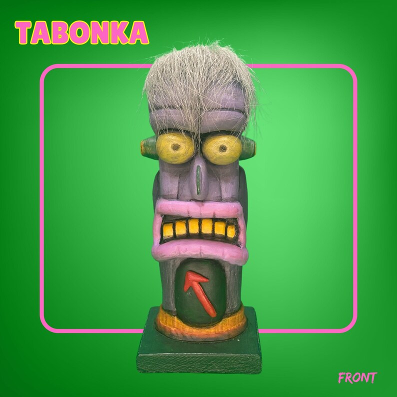 May include: A purple and green wooden tiki statue with a white hairpiece, yellow eyes, and a pink mouth with yellow teeth. The statue has a red arrow on its chest and the word "TABONKA" is written in yellow letters at the top of the image.