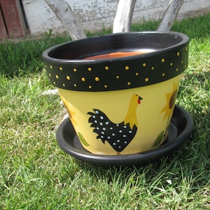 May include: A yellow ceramic planter with a black rim and black polka dots. The planter features a painted design of a black and white rooster with a red comb.