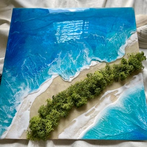 Pu&ograve; includere: Opera d'arte quadrata in resina raffigurante una scena di spiaggia. L'opera presenta vibranti onde blu e turchesi con schiuma bianca, una spiaggia sabbiosa e una striscia di muschio verde. Conchiglie sono posizionate attorno all'opera.
