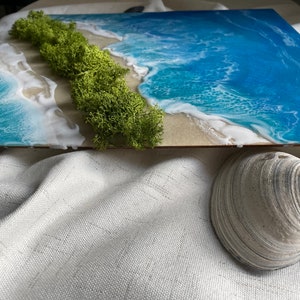 Pu&ograve; includere: Un'opera d'arte rettangolare raffigurante una scena di spiaggia con un oceano blu vibrante, onde bianche e schiumose e una striscia di sabbia. Il muschio verde rappresenta la terra. Una conchiglia si trova in primo piano, aggiungendo un elemento naturale al tema costiero.