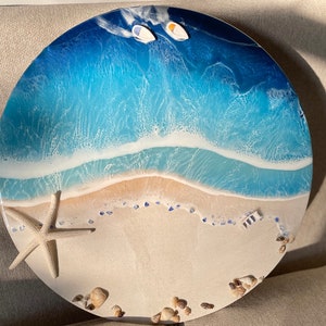 Pu&ograve; includere: Opera d'arte rotonda in resina raffigurante una scena di spiaggia. L'opera presenta una riva sabbiosa, onde schiumose in tonalit&agrave; di blu e due piccole barche. Una stella marina e conchiglie sono posizionate sulla sabbia. &Egrave; un oggetto decorativo.