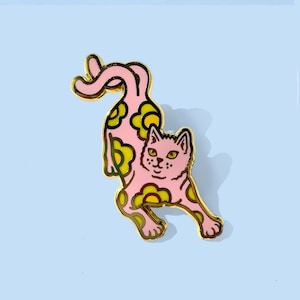 May include: A pink enamel pin of a cat with a yellow daisy pattern. The cat is in a playful pose with its tail curled up.