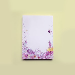 May include: A white notepad with a purple and yellow floral border. The border is made of pressed flowers and has a watercolour effect.