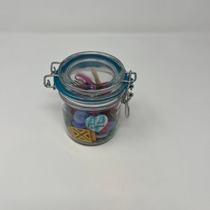 以下が含まれることがあります： 青い蓋と金属製の留め具が付いたガラスの瓶。瓶の中には、カラフルなボタン、ビーズ、そして「You are awesome」と書かれたハート型のチャームが入っています。
