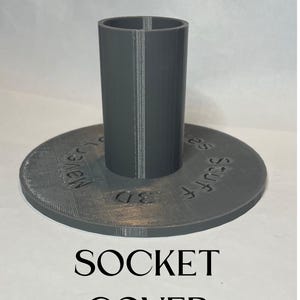 May include: A gray 3D-printed pool anchor socket cover. The cover has a cylindrical socket rising from a circular base. The text "POOL ANCHOR" and "SOCKET COVER" are printed above and below the object.