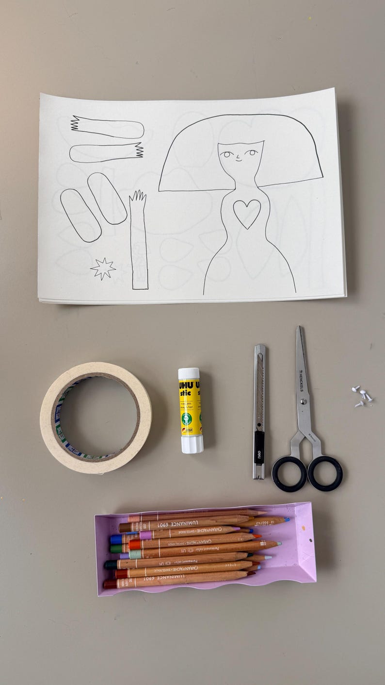 May include: A craft supplies arrangement featuring a paper doll outline, a roll of tape, glue stick, craft knife, scissors, a box of colored pencils, and small fasteners. The paper doll has a heart-shaped detail.