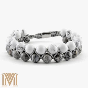 May include: A double-strand bracelet featuring alternating white and gray marble-like beads. The beads are strung on gray cord, with a silver-tone clasp. The bracelet is a neutral accessory.