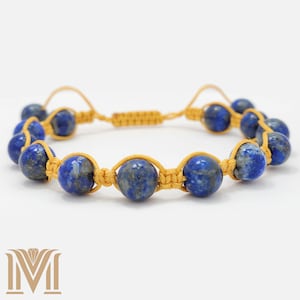 Peut inclure: Un bracelet en lapis-lazuli bleu avec un cordon doré. Le bracelet est noué et possède un nœud coulissant pour ajuster la taille.