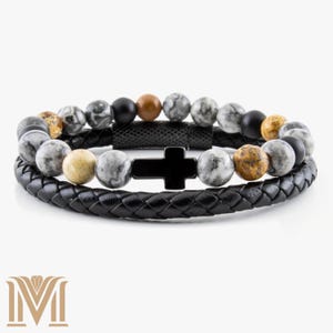 May include: A two-layer bracelet featuring a black leather band and a beaded strand. The top layer has a black cross, and the beaded strand includes gray, black, and brown stone beads. The bracelet is designed for a stylish accessory.