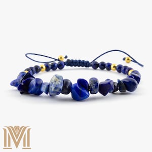 Op de afbeelding: Verstelbare armband met onregelmatige, diepblauwe lapis lazuli stenen afgewisseld met kleinere, ronde blauwe kralen en goudkleurige accenten. De armband is geregen op een donkerblauw koord.