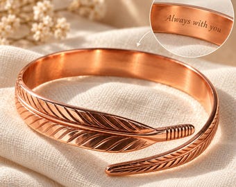 May include: A copper-toned metal cuff bracelet shaped like a feather that wraps around the wrist. The interior of the bracelet is engraved with the text Always with you, and the image includes a callout showing the engraving.