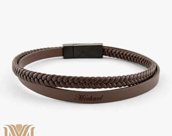 May include: A brown leather bracelet with a braided design and a silver clasp. The bracelet has the word "Michael" engraved on it.
