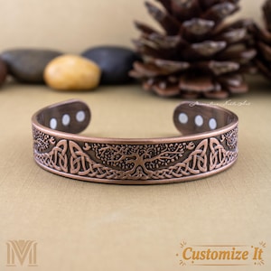 May include: A copper-colored cuff bracelet with a Celtic knot and tree of life design. The bracelet has three white magnetic dots on each end. The words "Customize It" are in the bottom right corner.
