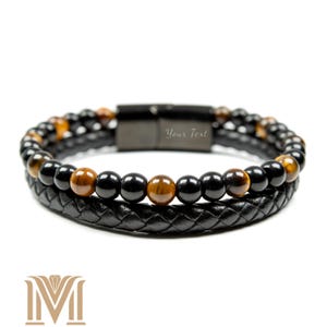 May include: A two-strand bracelet featuring black and brown beads, and a black braided leather band. The bracelet has a magnetic clasp with the text "Your Text" engraved on it. The beads are a mix of black onyx and tiger's eye.