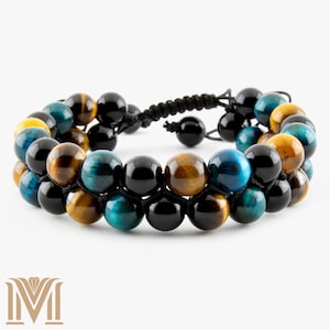 May include: Double-strand bracelet featuring a mix of round beads in black, blue, and golden-brown hues. The beads are strung on black cords, creating a layered effect. The bracelet has an adjustable closure.