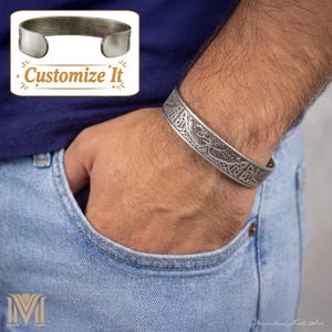 Könnte beinhalten: Ein silberfarbenes Armband mit einem komplizierten keltischen Knotenmuster. Das Armband wird am Handgelenk getragen, und das Bild zeigt auch eine blaue Jeans-Tasche und den Text "Customize It". Der Umfang des Armbands beträgt ca. 20 cm.