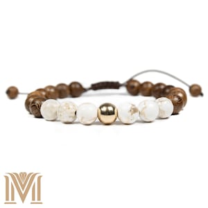 May include: A brown and white beaded bracelet with a gold accent bead. The bracelet is made with wooden and white stone beads.