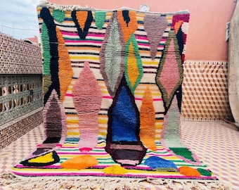 May include: A colourful Moroccan rug with a geometric pattern of diamonds and stripes. The rug is made of wool and has a fringe border.