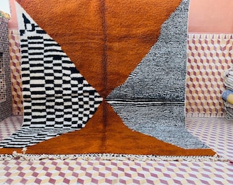 Può includere: Un grande tappeto rettangolare con un design geometrico. Il tappeto è realizzato in lana e presenta una combinazione di colori marrone, nero e bianco. Il tappeto è frangiato su tutti i lati.