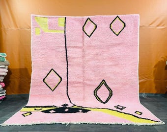 May include: A pink and yellow geometric patterned rug with black outlines. The rug has a fringe border.