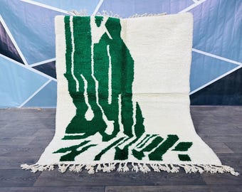May include: A white and green abstract rug with a fringe border. The rug has a modern design with a large green abstract shape on a white background.
