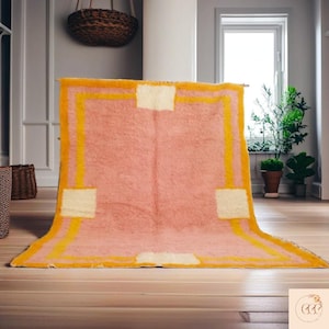 May include: A pink and yellow patterned rug with a white border. The rug has a fluffy texture and is laid out on a wooden floor.