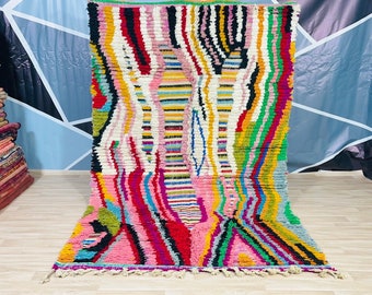 May include: A colourful Moroccan rug with a geometric pattern in shades of pink, green, yellow, blue, and black. The rug has a fringe border and is made of wool.
