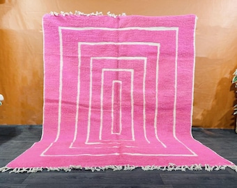 May include: Pink and white geometric patterned rug with a fringe border. The rug has a modern design with a series of white squares within a larger pink square.