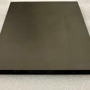 May include: A dark grey, rectangular, solid object with a smooth surface. The object is a uniform colour and appears to be made of a dense material. The edges are sharp and well-defined. The object is resting on a white surface.