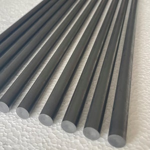 May include: A set of ten black carbon fiber rods. The rods are arranged in a row, with the ends of the rods aligned. The rods are smooth and have a slightly shiny finish.