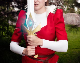 May include: A woman in a red and white costume holds a large, gold and white sword with a blue gem in the center. The sword has a white blade and a gold hilt.