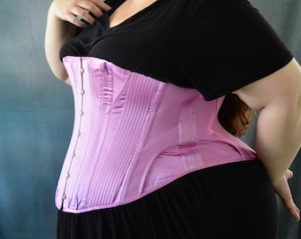 May include: A pink satin corset with a busk closure and a black skirt. The corset has a boned structure and a smooth, shiny finish.