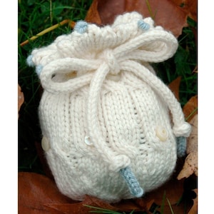 May include: A white knitted drawstring bag with a blue and white bow. The bag has a ruffled top and is decorated with white buttons.