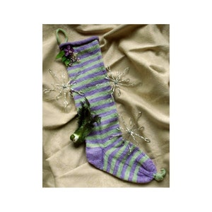 Könnte beinhalten: Ein gestrickter Strumpf in Lila und Grün mit einer Blumenverzierung und einem kleinen grünen Vogel-Anhänger.