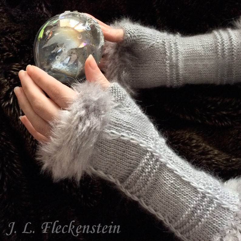 May include: A pair of gray knitted fingerless gloves with a fluffy white trim. The gloves are held in a person's hands, and a clear glass ball is in the background.