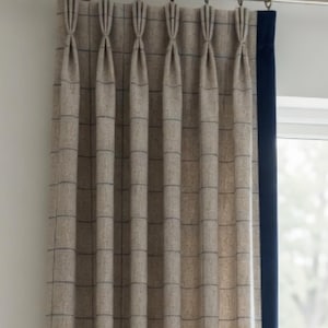 May include: A beige curtain with a dark blue grid pattern and pinch pleat header, suspended from a metallic curtain rod with rings. The curtain features a solid dark blue vertical border along the right edge, creating a structured appearance.