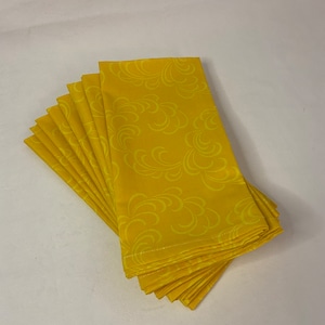 May include: A stack of ten yellow fabric napkins with a white swirl pattern.