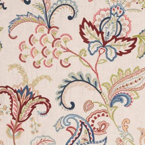 May include: Cream-colored fabric with an intricate floral pattern. The design features stylized flowers and leaves in shades of red, blue, pink, and green. The embroidery-like details create a textured appearance, suitable for home decor or apparel.