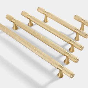 May include: Set of five gold-toned cabinet pulls with a textured finish. The pulls are in various sizes, ranging from small to large.