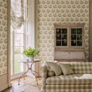 May include: A living room scene featuring a sofa with a green and white plaid pattern, complemented by matching throw pillows. The room includes a small round table, a cabinet, and a window with a floral patterned curtain and wallpaper.