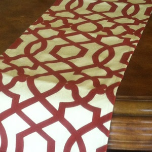 May include: A red and cream table runner with a geometric pattern. The runner is made of fabric and has a smooth texture.