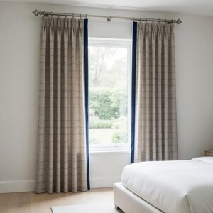 May include: A pair of floor-length pinch pleat curtains featuring a beige and brown grid pattern. Each curtain panel is accented with a solid navy blue vertical border along the inner edge and is suspended from a metallic curtain rod.