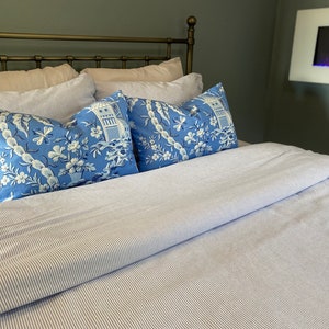 May include: A bed with a light blue and white striped comforter and matching pillows. The pillows are a vibrant blue with a white floral and pagoda design. The headboard is a dark metal.