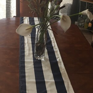 May include: A white and navy blue striped table runner with a vase of white calla lilies and brown branches.